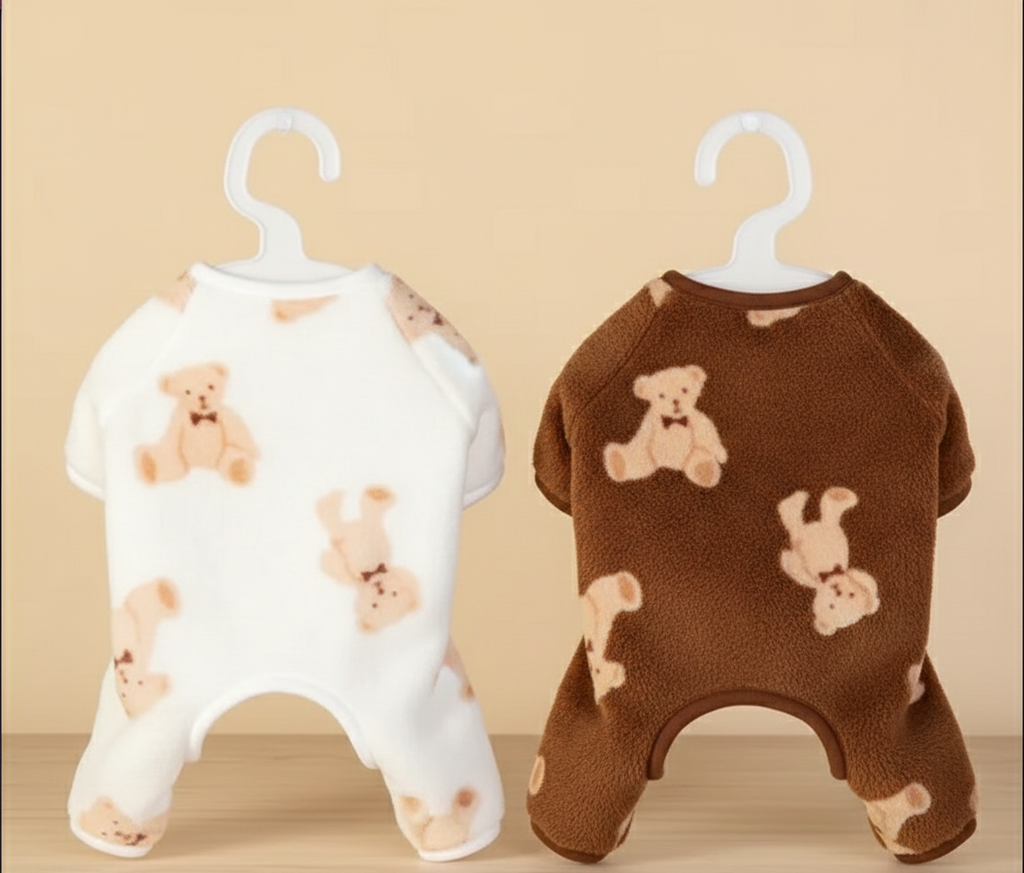 Two pet rompers with teddy bear patterns on hangers against a beige background