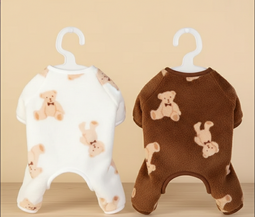 Two pet rompers with teddy bear patterns on hangers against a beige background